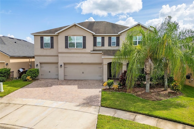 view of front of property featuring a front yard, decorative driveway, a garage, and stucco siding