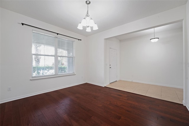 empty room featuring baseboards, an inviting chandelier, and wood finished floors