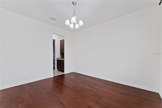 unfurnished room with visible vents, baseboards, a notable chandelier, and dark wood-style flooring