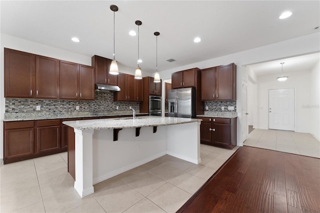 kitchen with visible vents, an island with sink, under cabinet range hood, appliances with stainless steel finishes, and light tile patterned floors