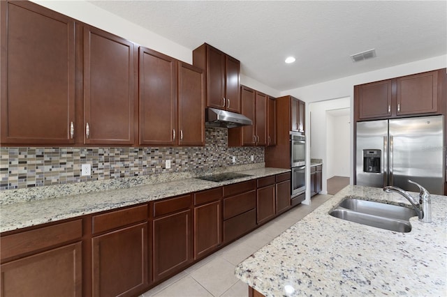 kitchen featuring light tile patterned floors, a sink, stainless steel appliances, under cabinet range hood, and backsplash