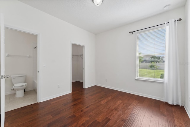 unfurnished bedroom featuring ensuite bathroom, baseboards, dark wood-style floors, and a spacious closet