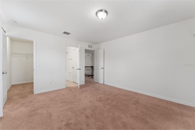 unfurnished bedroom featuring a spacious closet, visible vents, light colored carpet, and baseboards