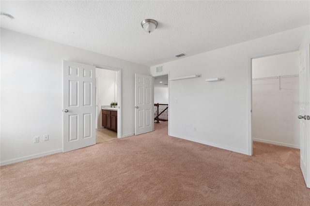 unfurnished bedroom featuring a walk in closet, light colored carpet, and visible vents