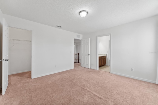 unfurnished bedroom with visible vents, a walk in closet, a textured ceiling, a closet, and light colored carpet