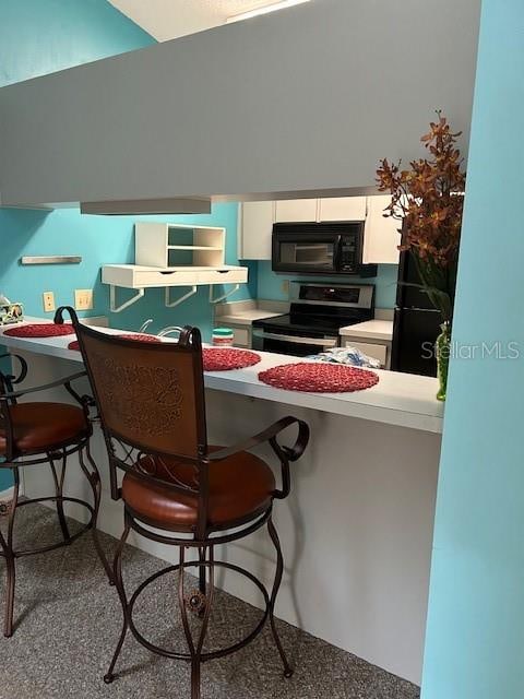 kitchen with white cabinetry, kitchen peninsula, electric range, and a breakfast bar area