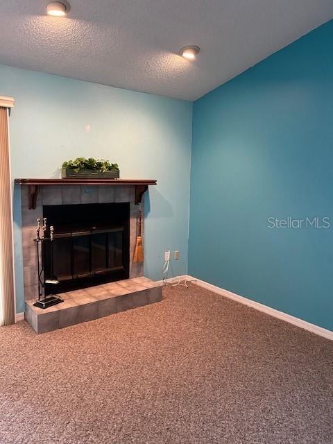 living room with a textured ceiling, a tile fireplace, and carpet floors