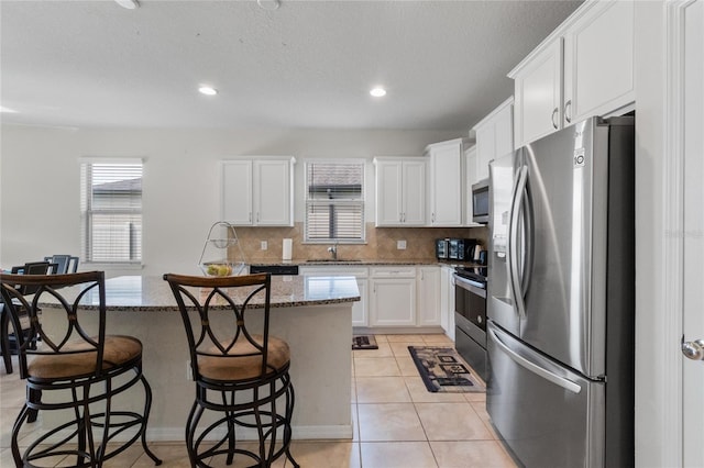 kitchen featuring appliances with stainless steel finishes, dark stone countertops, white cabinetry, and a center island