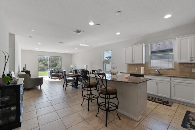 kitchen with white cabinets, a center island with sink, dark stone counters, and backsplash