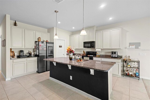 kitchen featuring dark stone countertops, decorative light fixtures, a kitchen breakfast bar, black appliances, and an island with sink