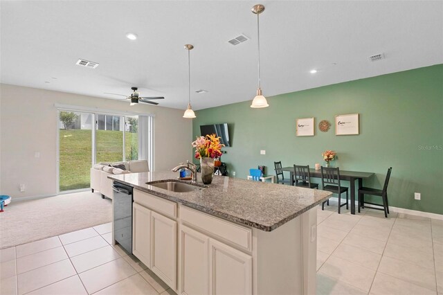 kitchen featuring pendant lighting, light stone counters, sink, ceiling fan, and a center island with sink