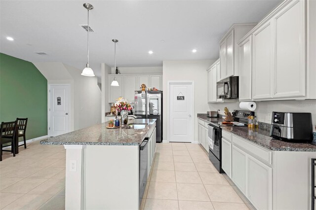 kitchen with light tile patterned floors, hanging light fixtures, appliances with stainless steel finishes, a center island with sink, and white cabinets