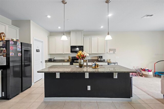 kitchen with black appliances, a breakfast bar area, stone countertops, and a kitchen island with sink