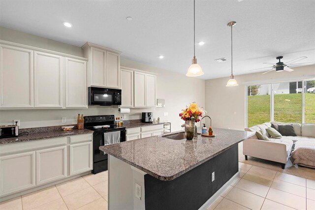 kitchen with sink, black appliances, light tile patterned flooring, ceiling fan, and a center island with sink