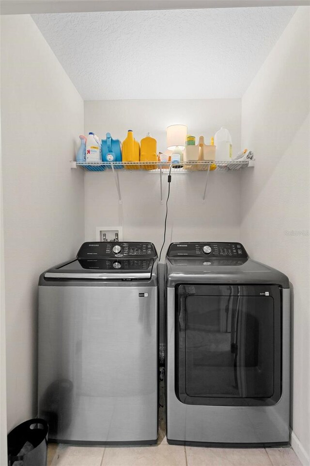 laundry area featuring washing machine and clothes dryer, light tile patterned floors, and a textured ceiling