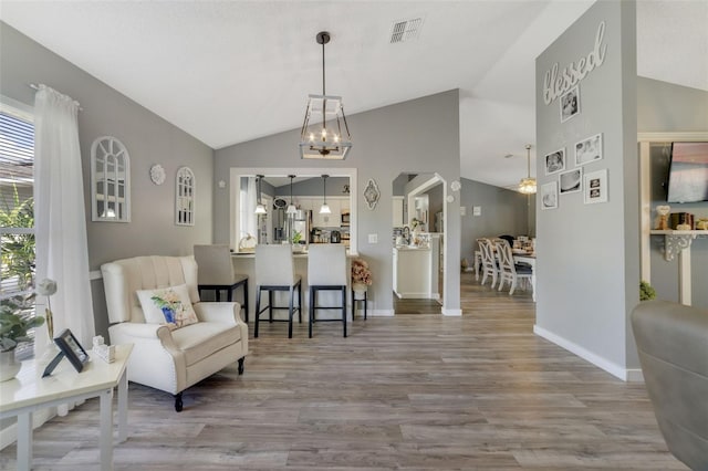 living area with an inviting chandelier, vaulted ceiling, and light hardwood / wood-style floors