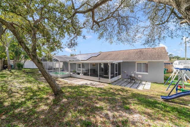 rear view of property featuring a patio area, glass enclosure, a playground, a yard, and a fenced in pool