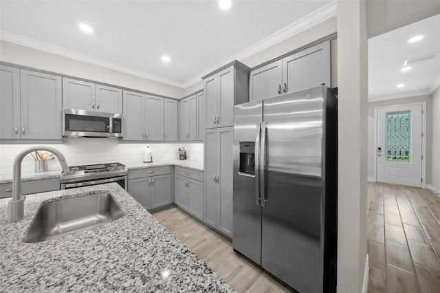 kitchen featuring light wood-type flooring, appliances with stainless steel finishes, light stone countertops, and sink