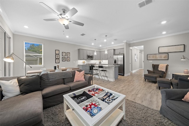 living room with light wood-type flooring, ceiling fan, crown molding, and sink