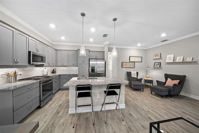 kitchen featuring a center island with sink, pendant lighting, light hardwood / wood-style flooring, appliances with stainless steel finishes, and gray cabinets