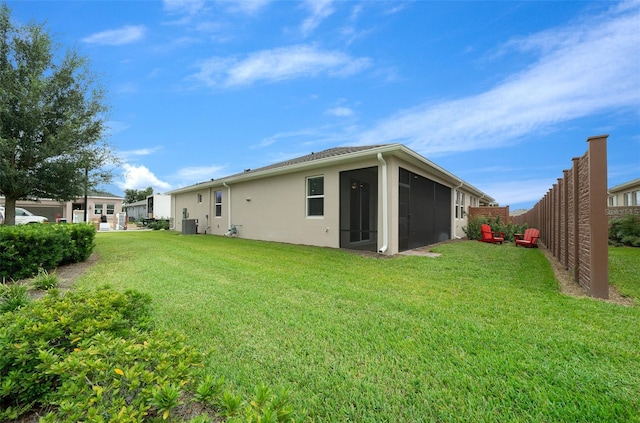 rear view of property with a sunroom, a lawn, and central AC