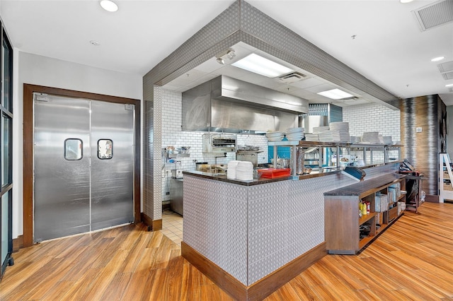 kitchen with built in refrigerator, kitchen peninsula, backsplash, and light hardwood / wood-style floors