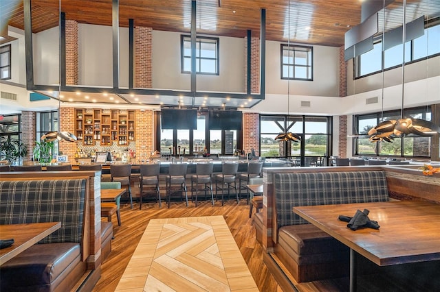 dining area with wood ceiling, a healthy amount of sunlight, a high ceiling, and hardwood / wood-style floors