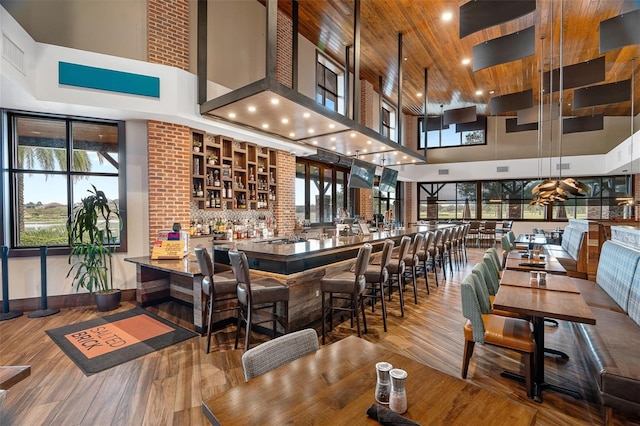 dining area featuring a towering ceiling, wood ceiling, wood-type flooring, and bar