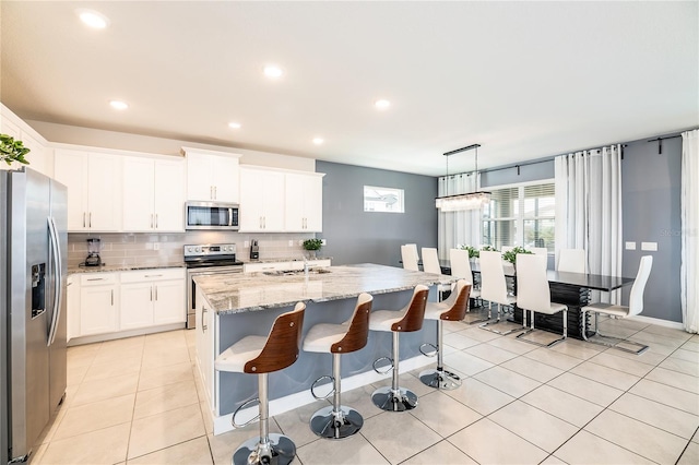 kitchen featuring appliances with stainless steel finishes, white cabinetry, an island with sink, and hanging light fixtures