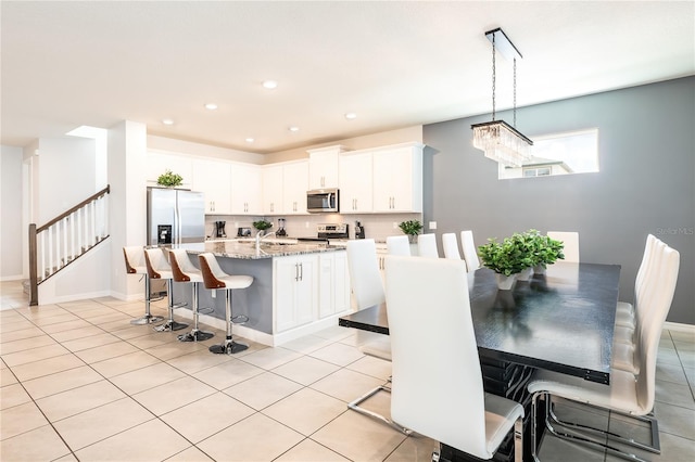 kitchen with stainless steel appliances, a kitchen breakfast bar, light stone countertops, a center island with sink, and white cabinets