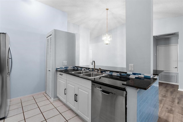 kitchen with decorative light fixtures, stainless steel appliances, sink, white cabinets, and light hardwood / wood-style floors