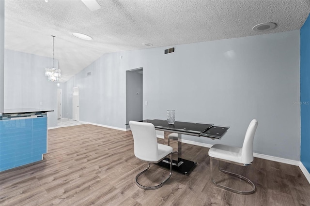 dining area featuring wood-type flooring, vaulted ceiling, and a textured ceiling