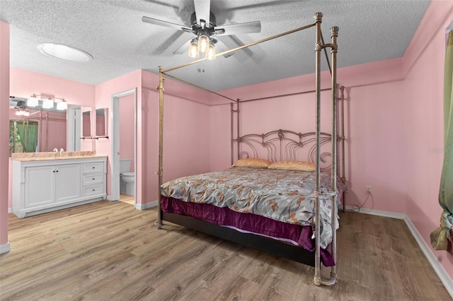 bedroom featuring a textured ceiling, light hardwood / wood-style floors, ceiling fan, and connected bathroom