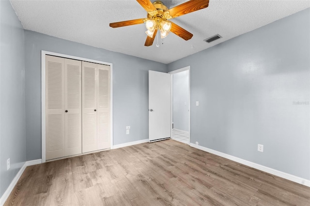 unfurnished bedroom with light wood-type flooring, a textured ceiling, ceiling fan, and a closet