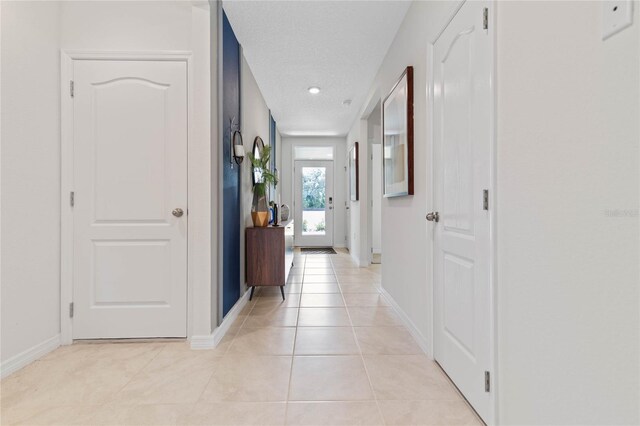 hallway with a textured ceiling and light tile patterned floors