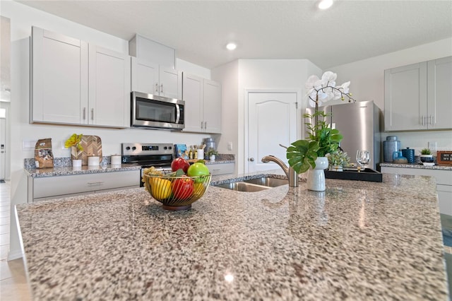 kitchen featuring light stone countertops, stainless steel appliances, sink, and a center island with sink