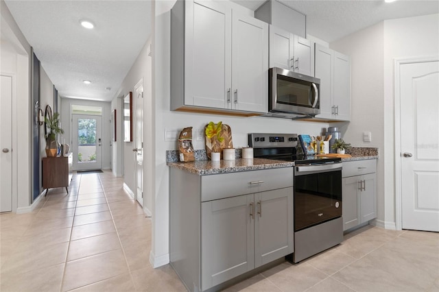 kitchen featuring dark stone countertops, a textured ceiling, light tile patterned floors, stainless steel appliances, and gray cabinetry