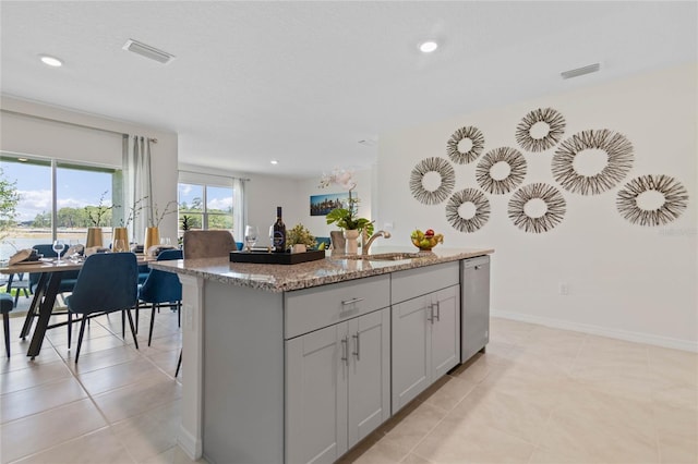 kitchen featuring light tile patterned floors, dishwasher, light stone counters, sink, and a center island with sink