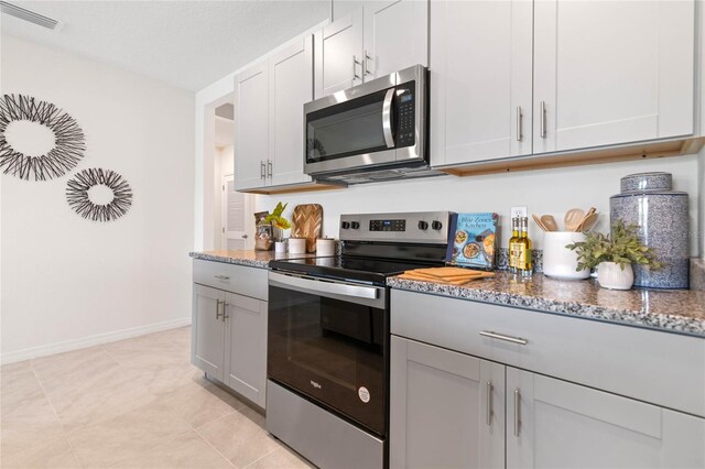 kitchen with gray cabinets, appliances with stainless steel finishes, light tile patterned flooring, and stone counters