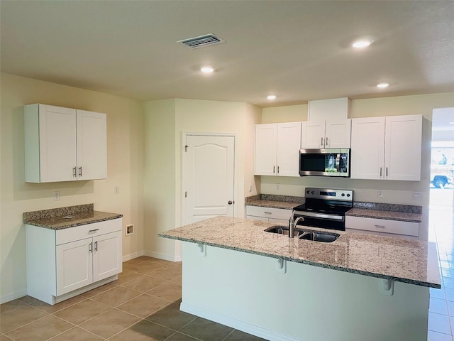 kitchen with visible vents, a breakfast bar area, light stone counters, stainless steel appliances, and a sink