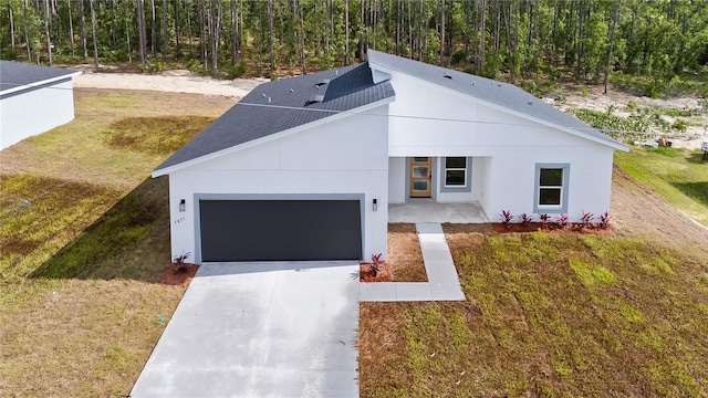 view of front of home featuring a wooded view, an attached garage, stucco siding, concrete driveway, and a front lawn