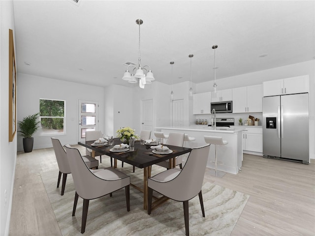 dining space with a notable chandelier, sink, and light wood-type flooring