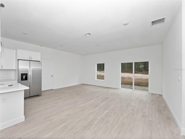 unfurnished living room with light wood-style flooring, baseboards, and visible vents