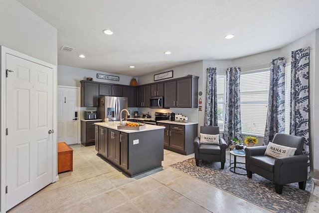 kitchen featuring a center island with sink, light tile patterned floors, stainless steel appliances, sink, and dark brown cabinetry