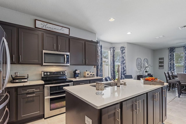 kitchen with appliances with stainless steel finishes, decorative backsplash, a center island with sink, and dark brown cabinets