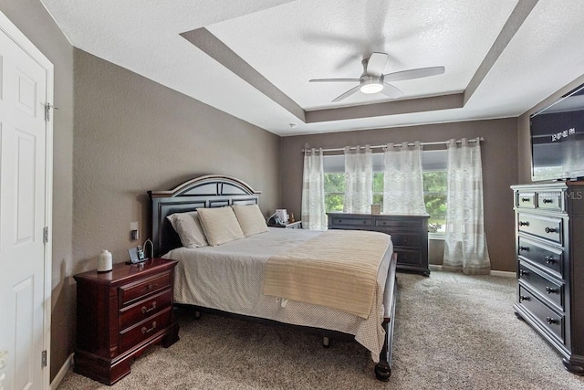 bedroom featuring a tray ceiling, a textured ceiling, ceiling fan, and carpet floors