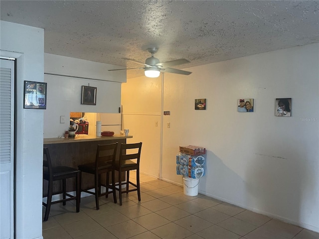 dining room with ceiling fan, bar, a textured ceiling, and light tile patterned floors