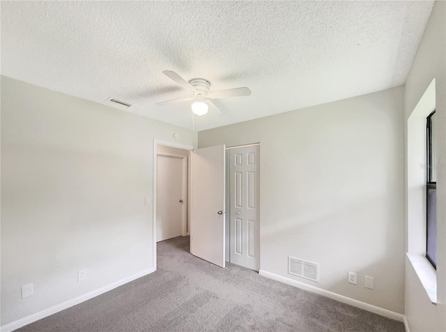 unfurnished bedroom with a textured ceiling, light colored carpet, ceiling fan, and a closet