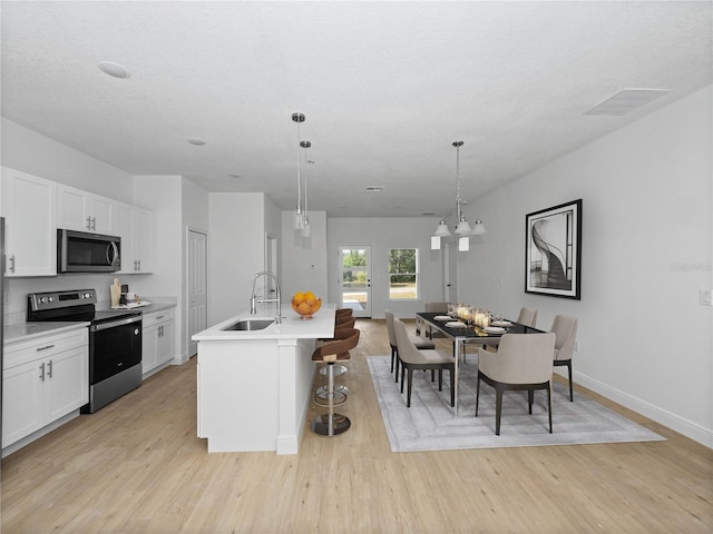 kitchen with white cabinets, light hardwood / wood-style flooring, appliances with stainless steel finishes, sink, and a kitchen island with sink