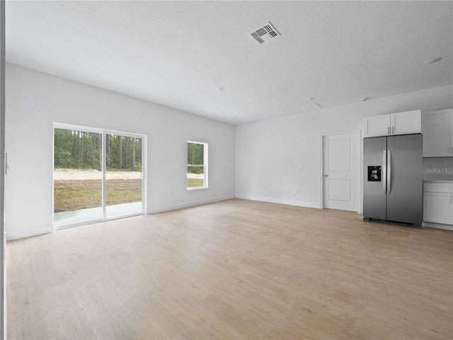 unfurnished living room with a textured ceiling, baseboards, visible vents, and light wood-type flooring